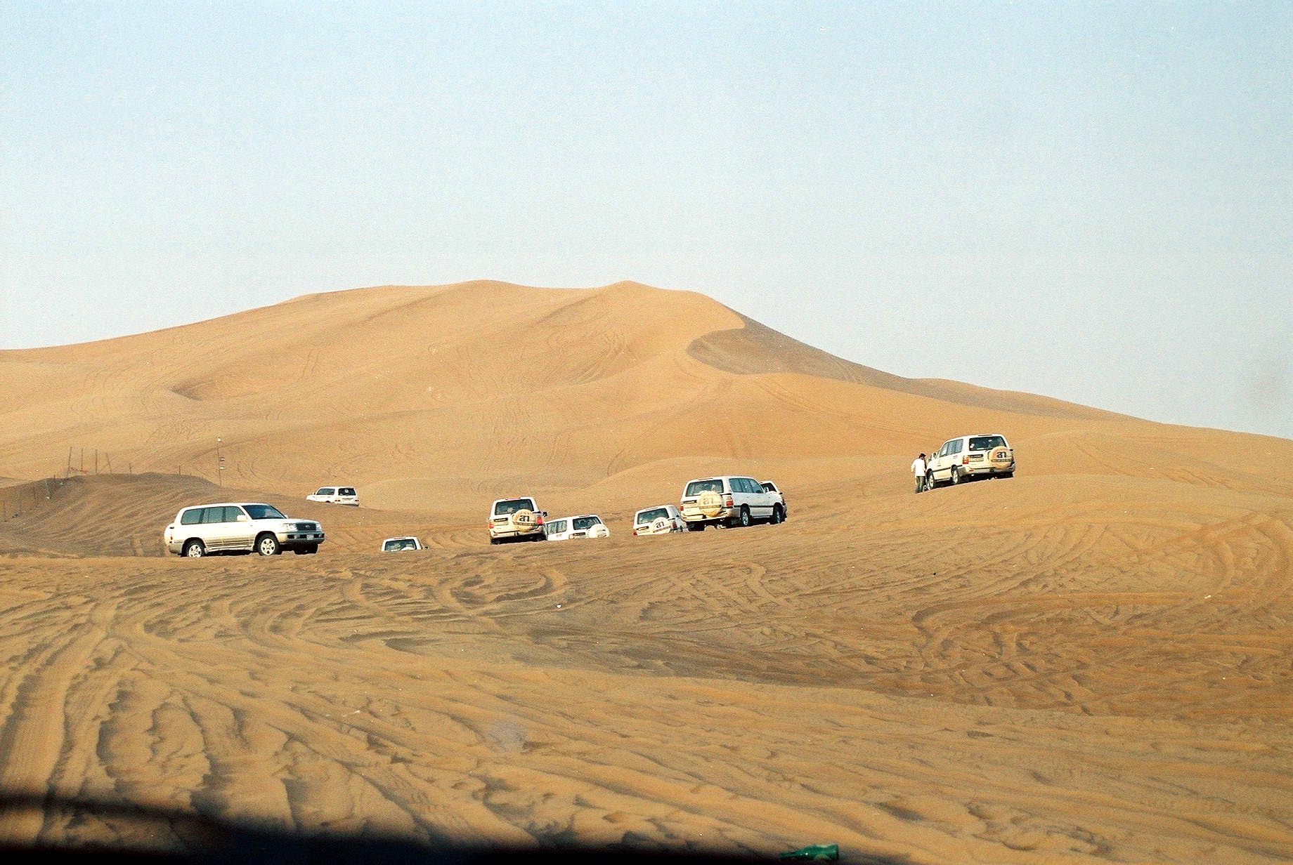 Convoys of land cruisers approaching a big dune